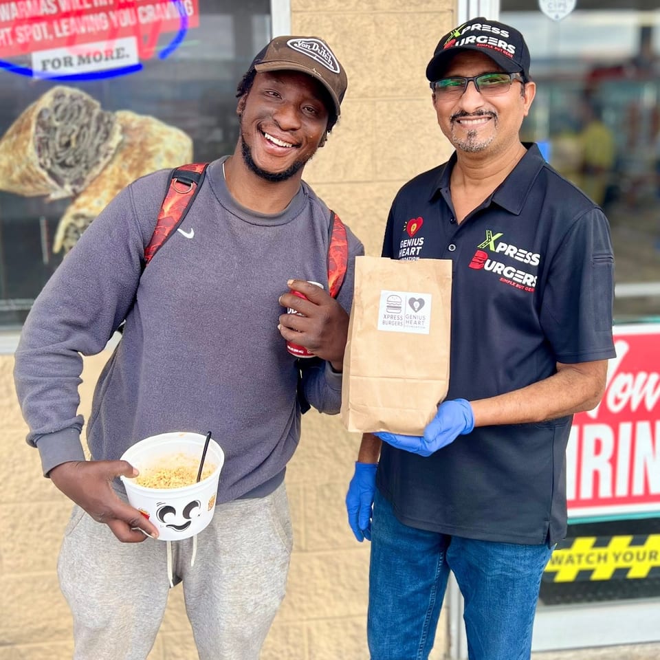 Two smiling people pose outside Xpress Burgers, holding a branded takeout bag and a cup of noodles.