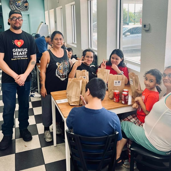 A diverse group gathers around a restaurant table with takeout bags and drinks, while several people pose and smile.