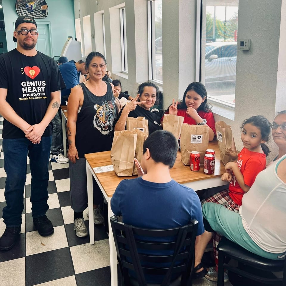 A diverse group gathers around a restaurant table with takeout bags and drinks, while several people pose and smile.