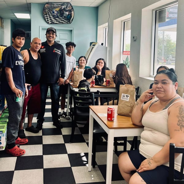 Family and friends gather inside Xpress Burgers, posing near tables with branded takeout bags and drinks on a checkered floor.