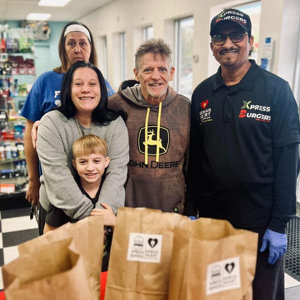 Five people, including an Xpress Burgers employee, stand behind several branded paper bags on a checkered floor.