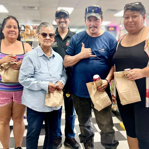 Five people, holding brown paper bags and drinks, stand together in a store aisle.