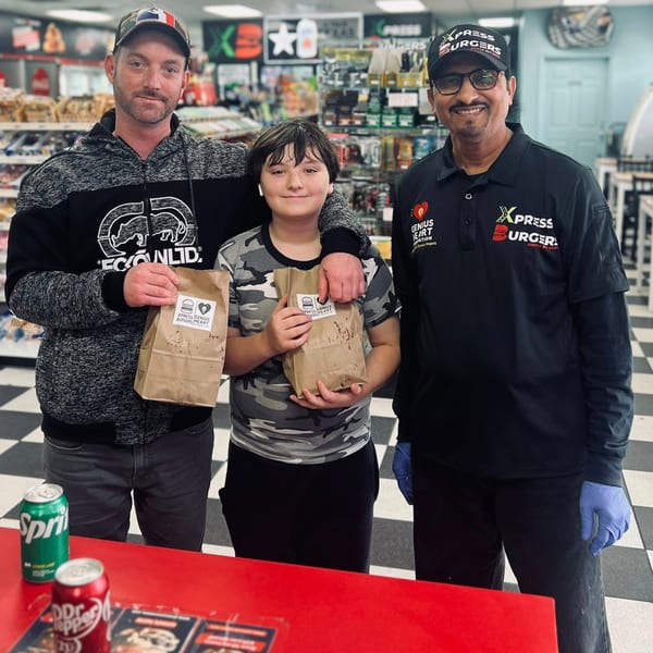 Two customers and an Xpress Burgers employee smiling with takeout bags in a store.