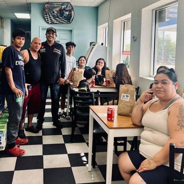 A group of people, including children, standing and sitting in a burger restaurant with checkered floors.
